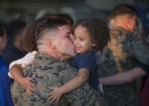 Service member kissing his children. 