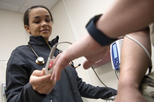 Service member wearing black zip-up takes pulse of patient's finger.