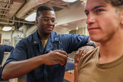 Uniformed Sailor gives flu shot to seated Sailor.