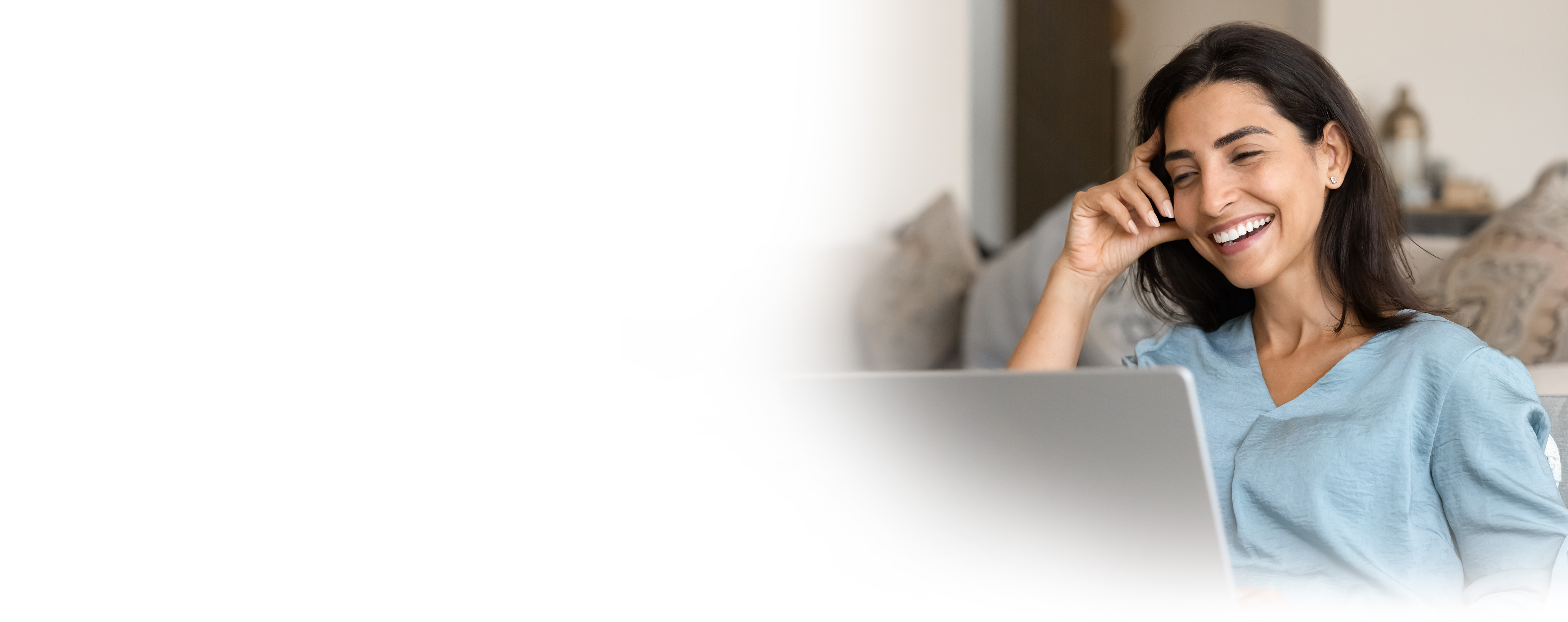 Woman smiling at laptop while sitting on a couch